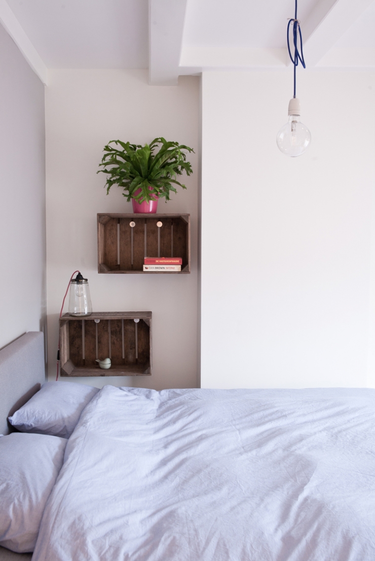 Naast het bed hangen houten kratjes, ideaal om boeken in op te bergen. De lamp is van I am Recycled. 